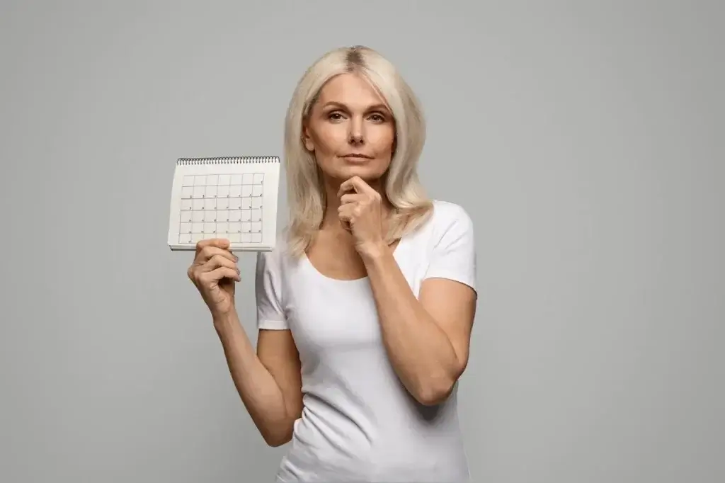 Pensive mature woman holding blank menstrual calendar, thinking about menopause and irregular periods.